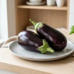 Twee verse paarse aubergines op een lichte keramische plaat; aubergine gezond